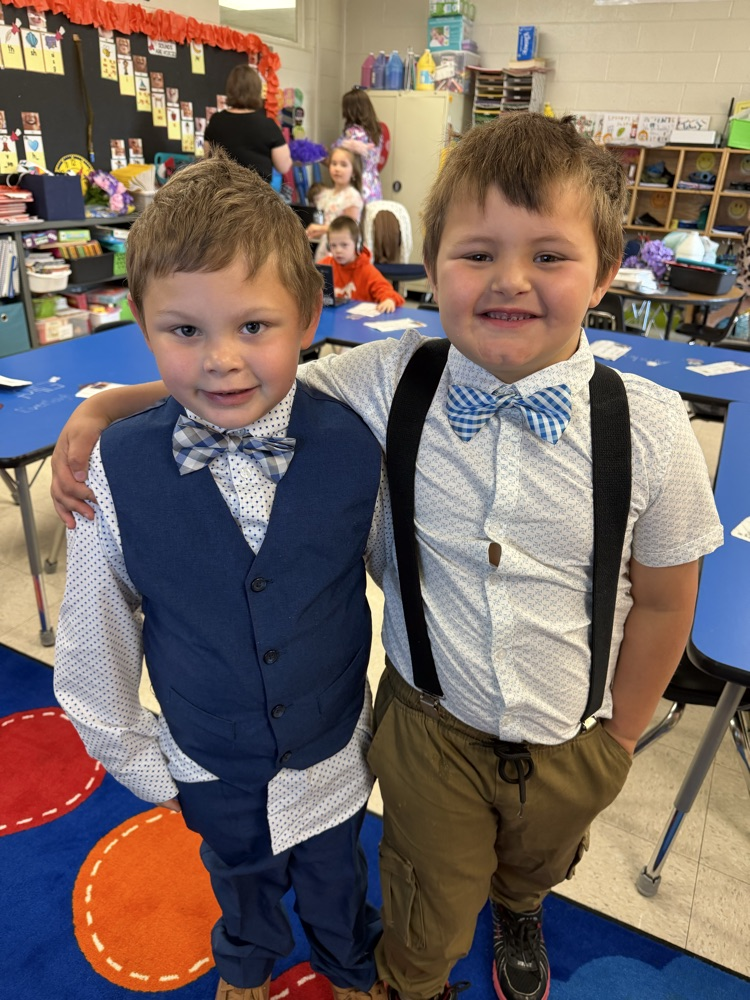 Two boys are dressed up for Johnson derby day. The boy on the left has on a button down shirt with blue vest and bow tie. the boy on the right has his arm around the other boy and is wearing a short sleeved button down w/ black suspenders and bow tie