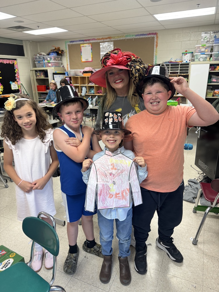 Children wearing self-made Derby hats smile for a picture with their teacher  