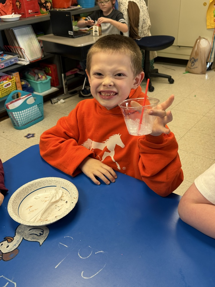 A boy smiles and holds up a cup of mint punch  