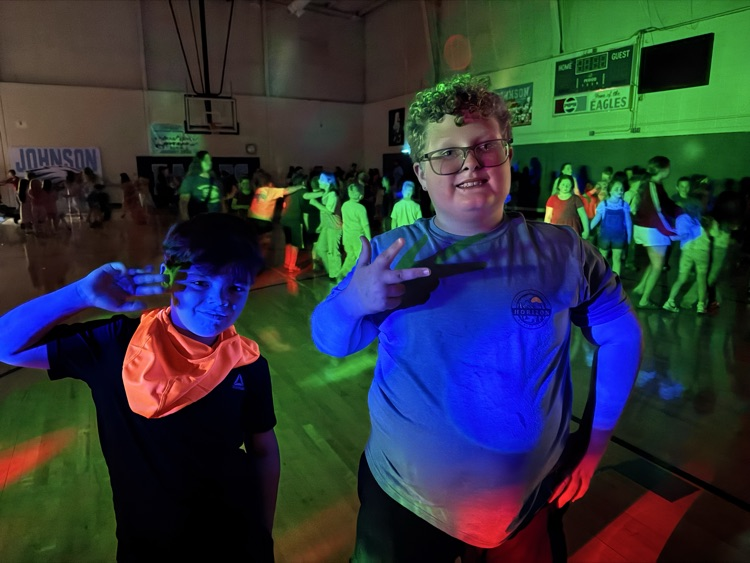 Two boys stand together in the school gym, which is darkened for the school dance. 