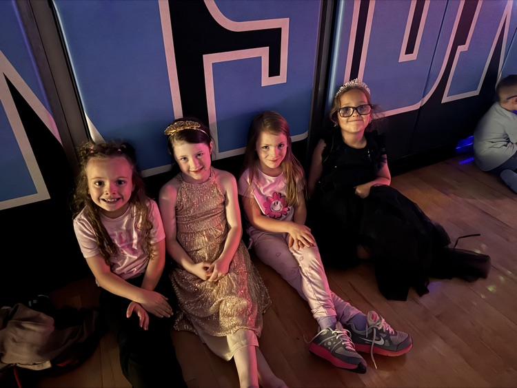 Four girls sit against the basketball wall mats in the gym  