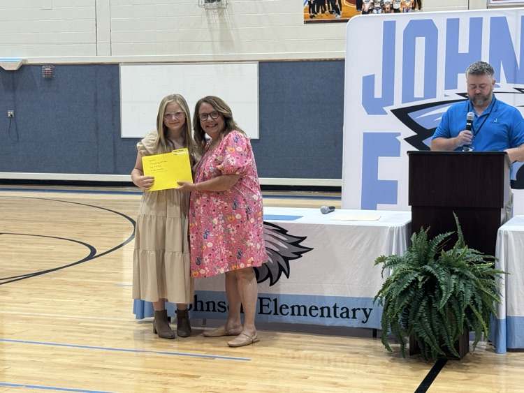 A teacher presents an award to her student in the gym