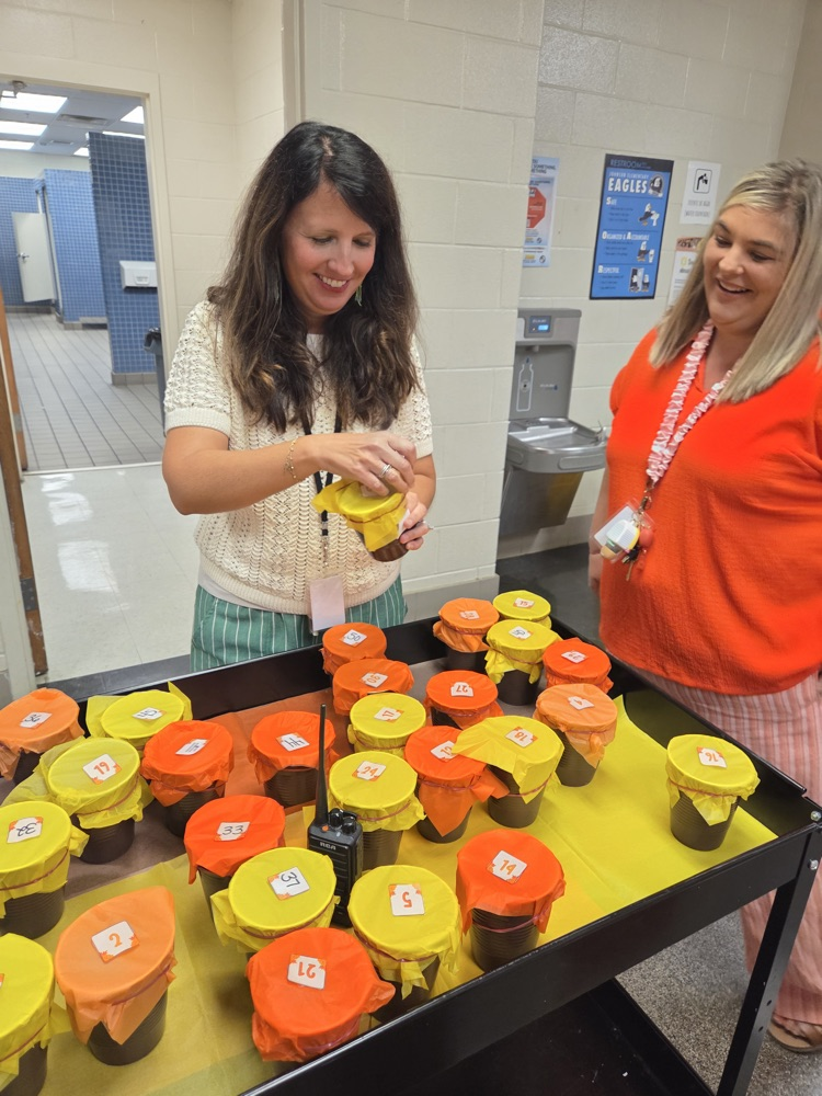 A teacher holds a plastic cup with her prize inside while another staff member looks on from the right. In the foreground, a cart loaded with yellow and orange cups can be seen  