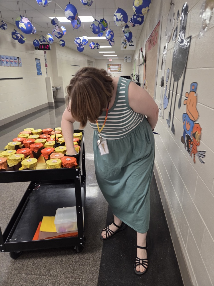 A teacher in a green dress looks down at the cup-filled cart while choosing her prize  