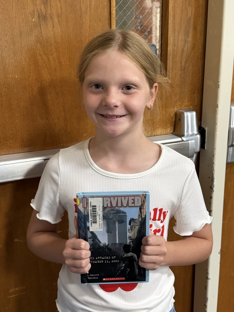 A young girl in a white shirt holds the book I Survived the Attacks of September 11by Lauren Tarshis  