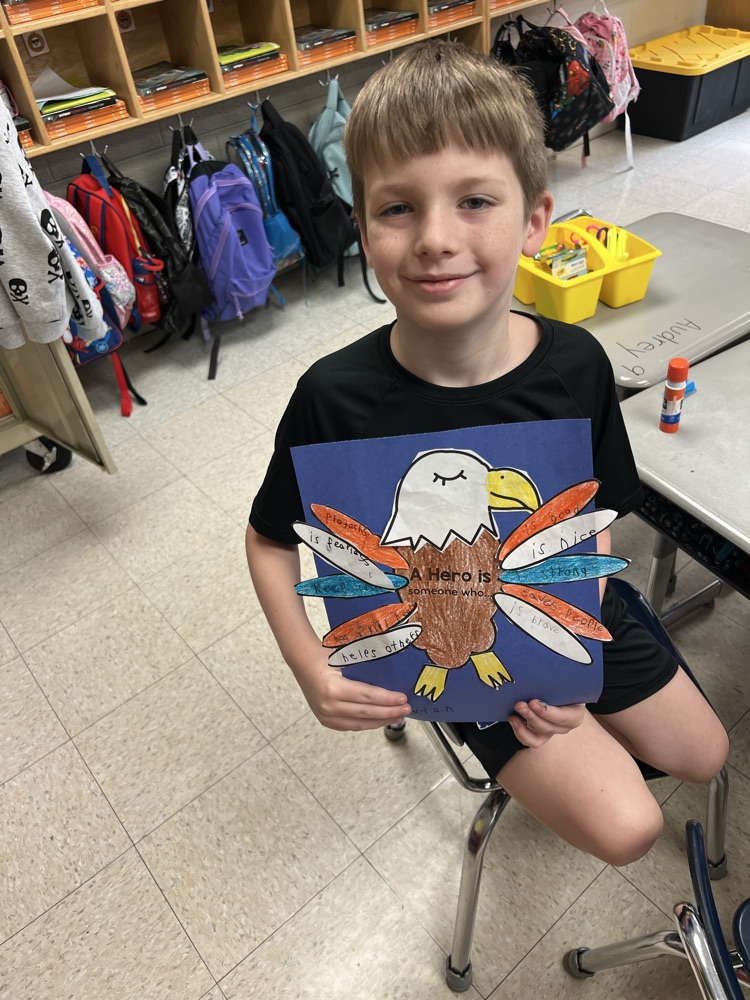 A boy smiles while holding his red, white, and blue eagle project highlighting the characteristics of a hero  