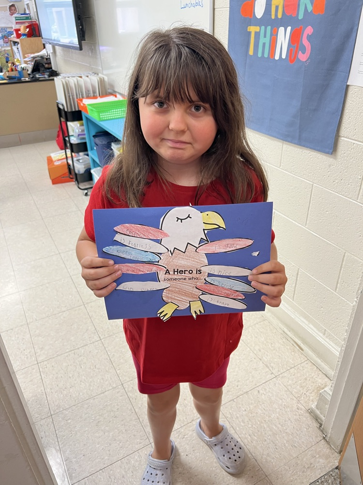 A girl smiles while holding her red, white, and blue eagle project highlighting the characteristics of a hero. 