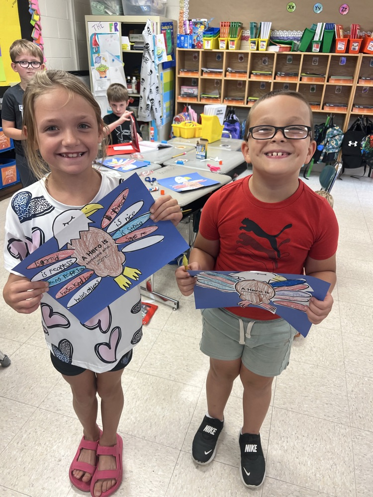 A boy and girl smile while holding their red, white, and blue eagle projects highlighting the characteristics of a hero. 