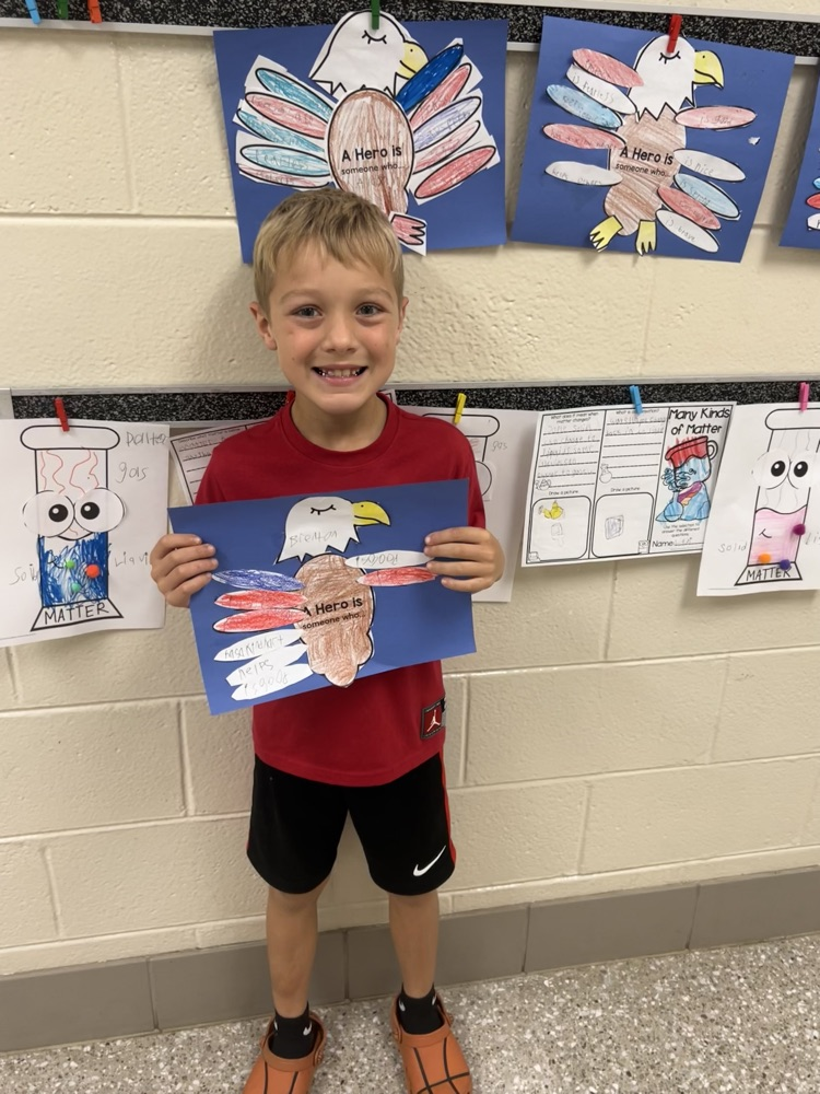 A boy smiles while holding his red, white, and blue eagle project highlighting the characteristics of a hero. 