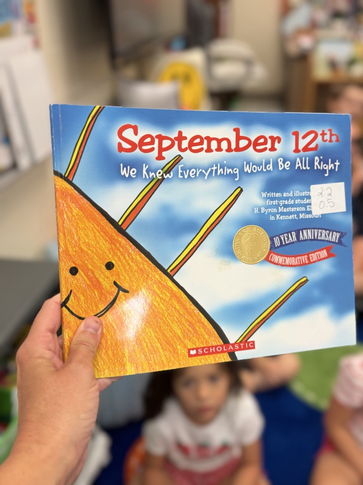 A hand is shown holding up the book September 12th: We Knew Everything Would Be Alright  