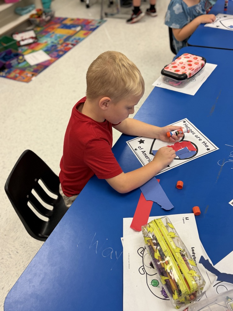 A boy sits at a blue table working on his torn paper heart project. 