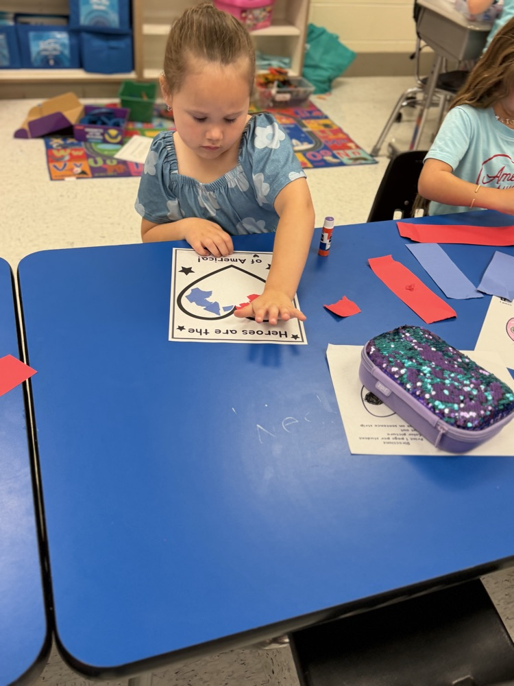 A girl sits at a blue table working on her torn paper heart art project  