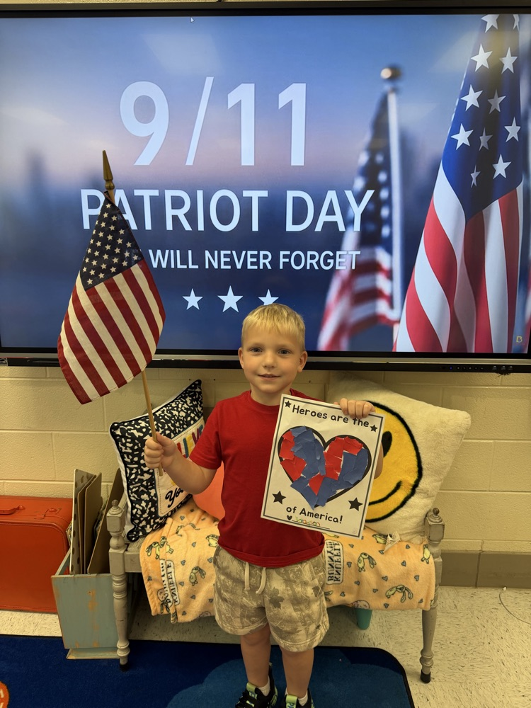 A boy in a red shirt holds up an American flag and his torn paper heart art project  