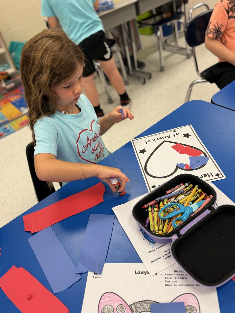 A girls sits at a blue table working on her torn paper heart art project  