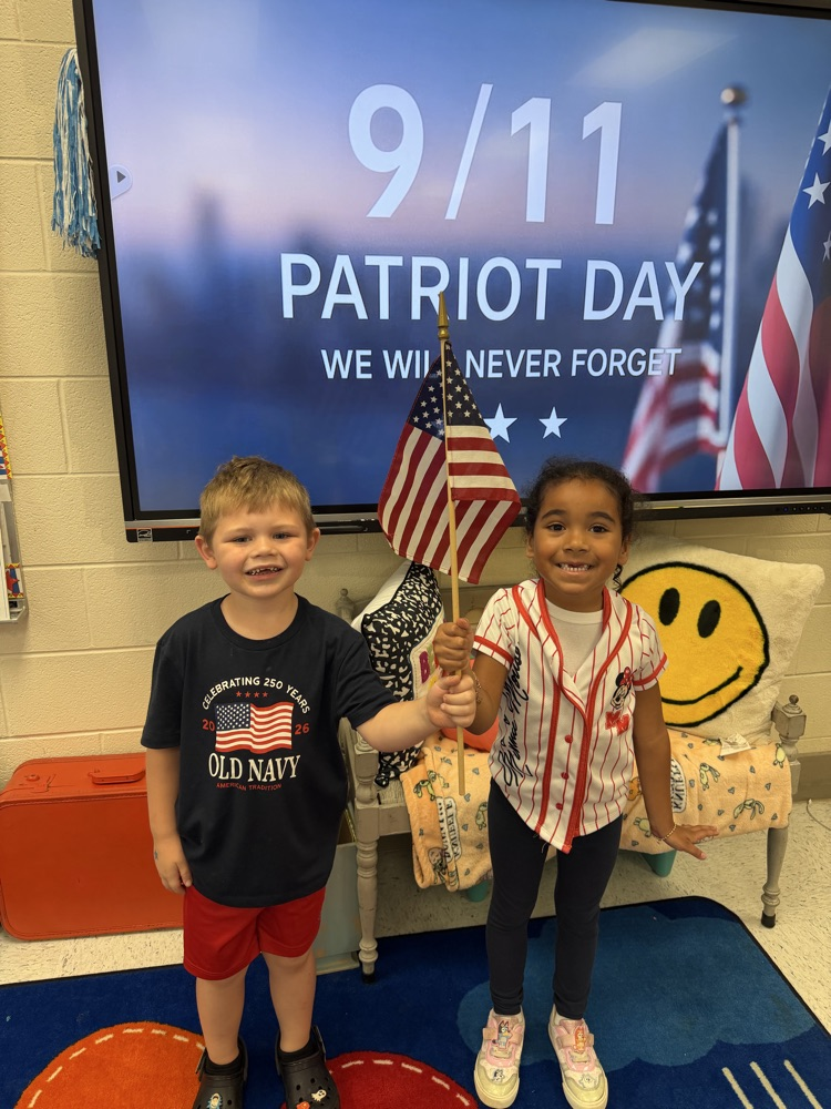 A boy and girl stand together holding an American flag between them. Behind them, a ViewSonic board displays patriotic imagery  