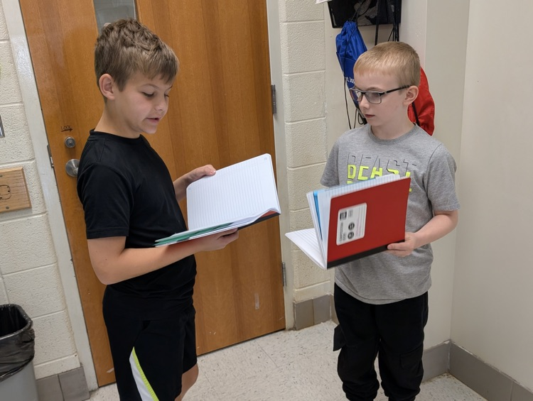 two boys staying together, reading their notes for class from their notebooks.