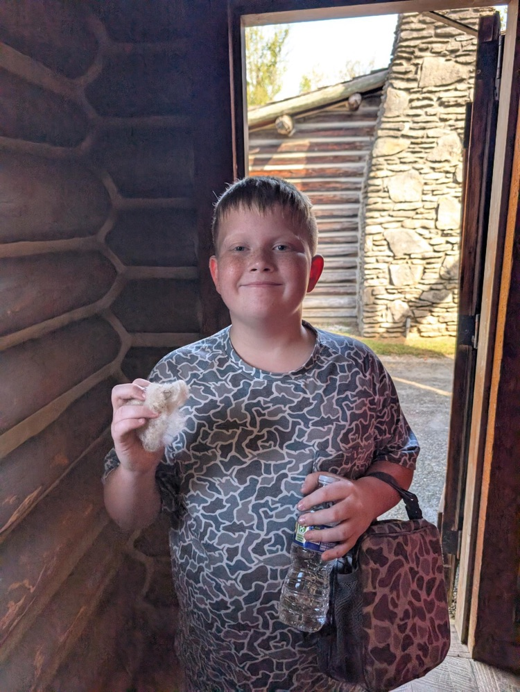 A boy in a camouflage shirt holds a water bottle in one hand and a piece of wool in the other.