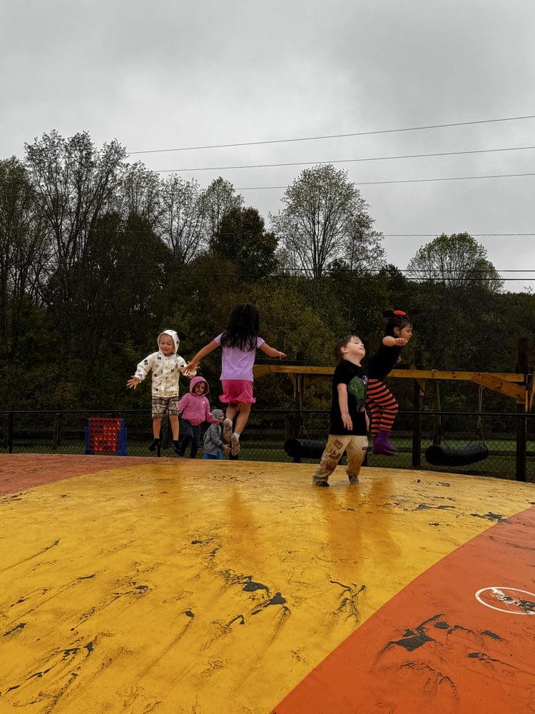 four children bounce on top of an orange and yellow, jumping pillow.
