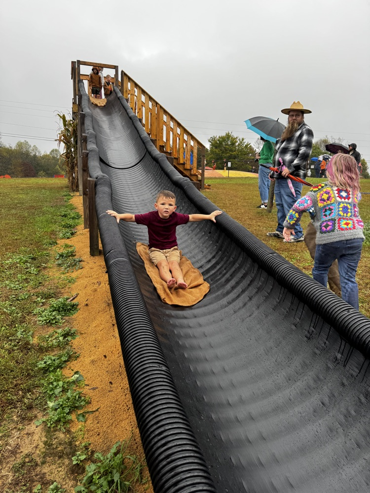 A boy slides down a large black slide while sitting on an orange towel.