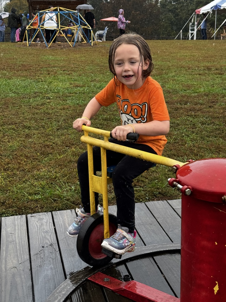 A girl in an orange T-shirt rides a unicycle that is attached to a fulcrum  