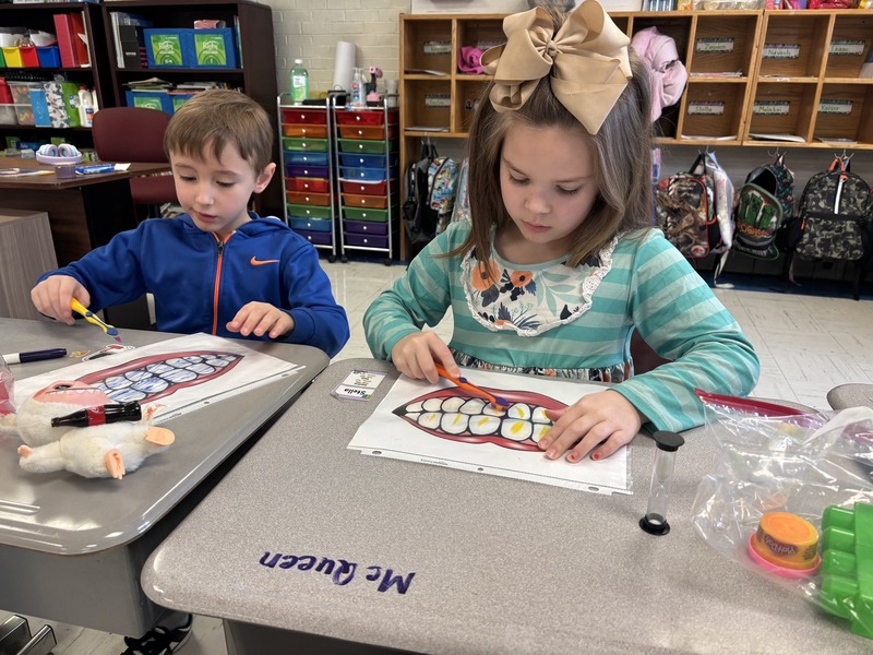 Two students erasing marker off their dirty laminated teeth with toothbrushes