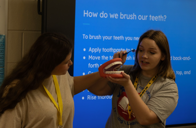 Two CFI students showing how to properly brush your teeth on a prop