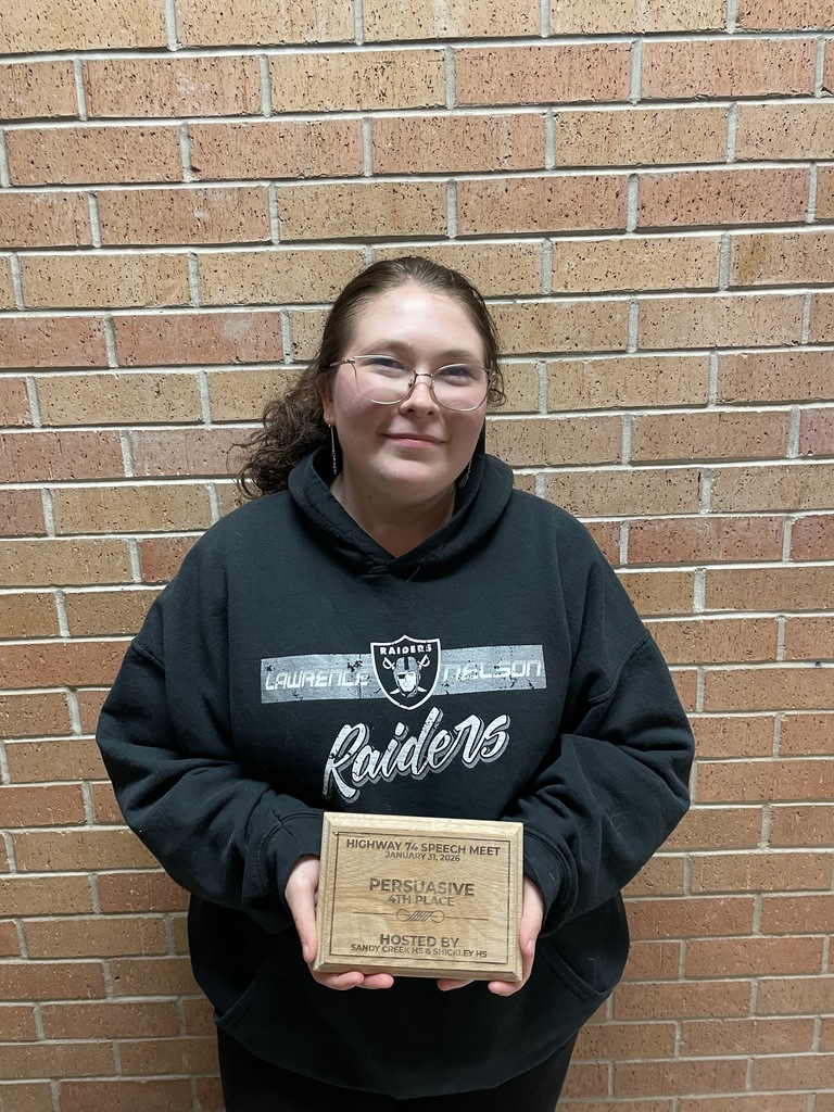 Natalie Jacobitz stands in a black hoodie against a brick wall with a plaque.