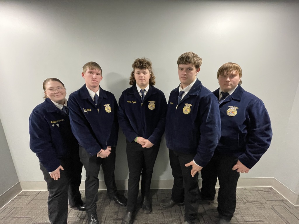 Five teenagers in FFA jackets and black pants stand against a gray wall