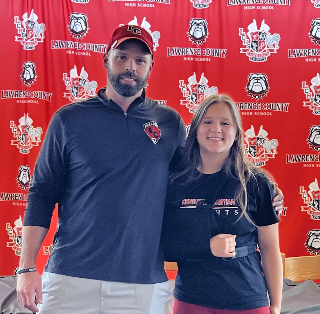 Man and woman in sports attire pose together in front of a red background with a logo.