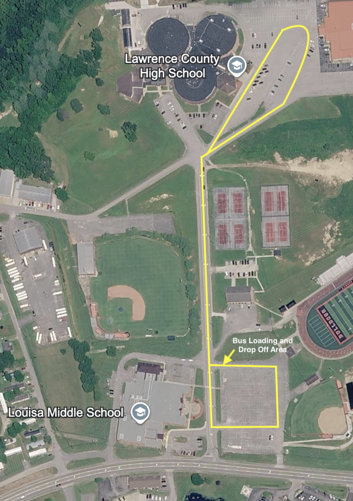 An aerial view of a school area shows a football field, a school building, and a bus loading area.