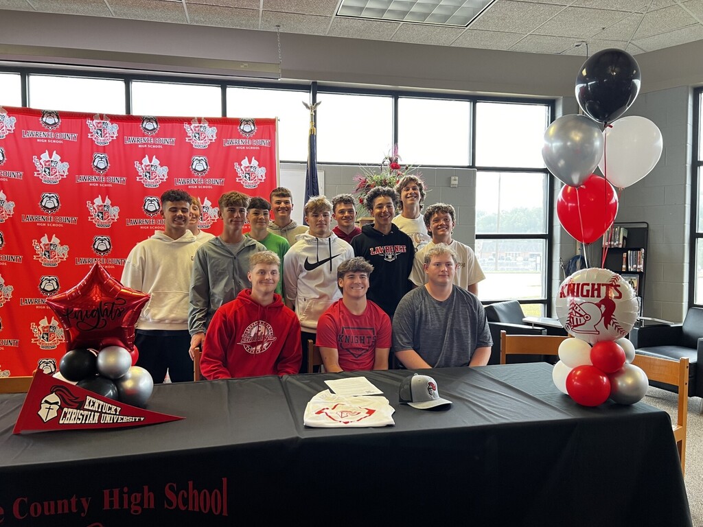 A group of people wearing red shirts at a signing event. Behind them is a red backdrop.