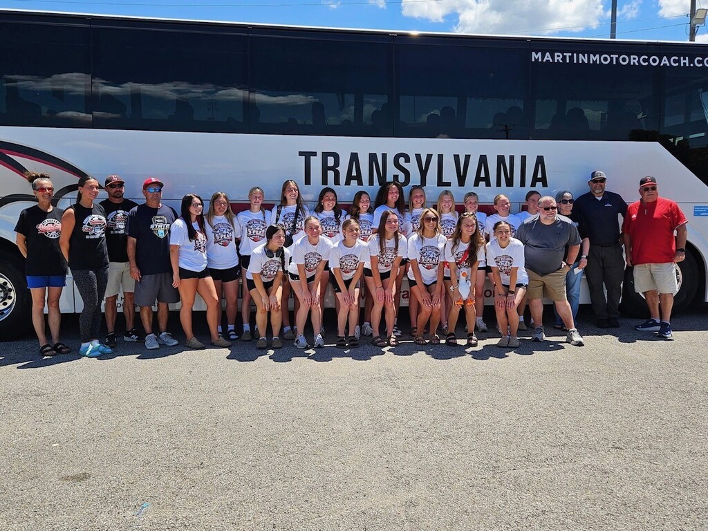 A group of people wearing white shirts pose for a photo in front of a bus.