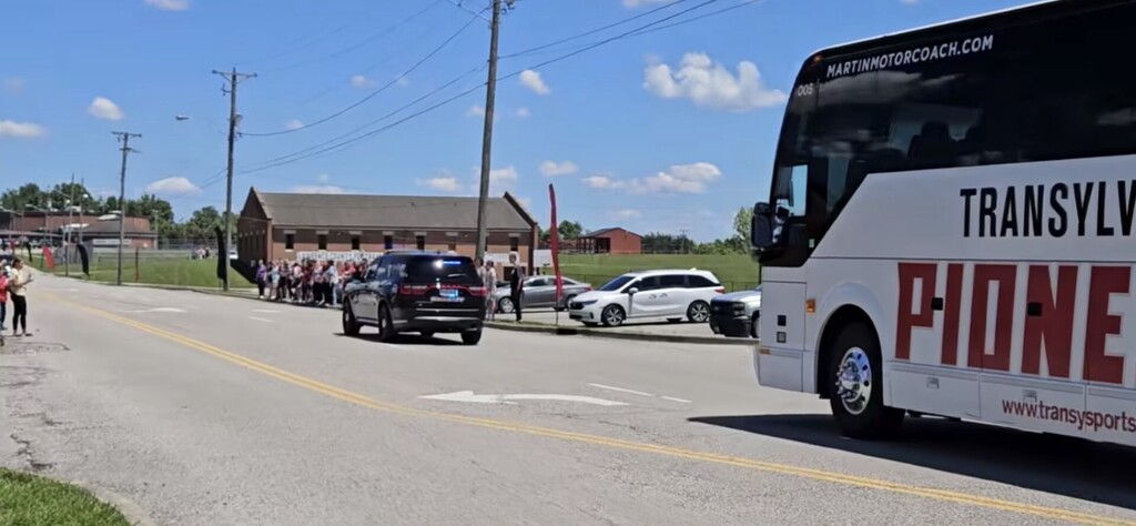 A bus with "Transyl" and "PIONE" texts on the side on a road with parked cars and people.