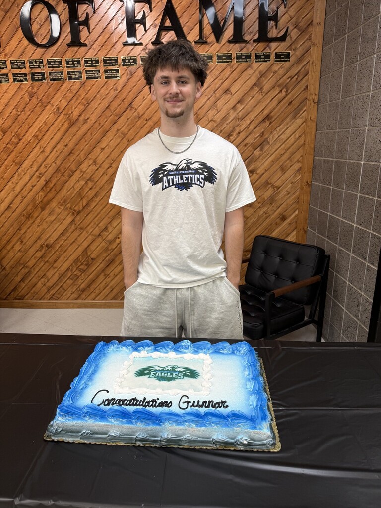 Man in a white t-shirt stands next to a table with a cake that says "Congratulations Gunner".