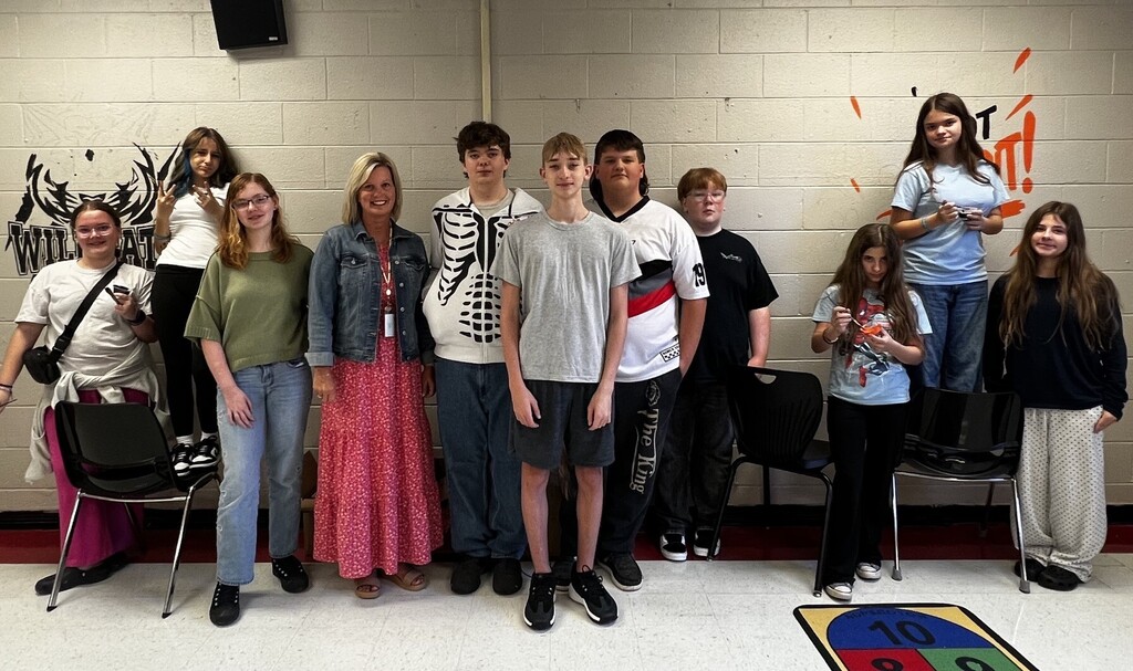 Nine students and a teacher in casual clothing pose in a classroom with graffiti on the wall.