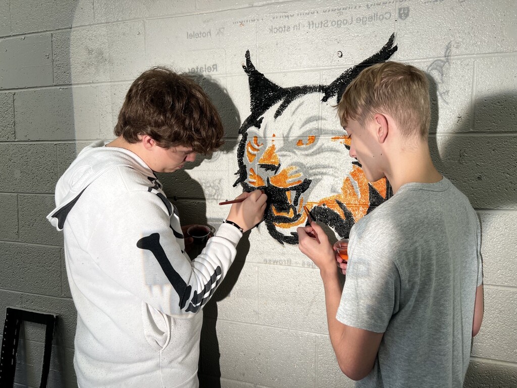Two young men are working on a large mosaic of a tiger on a white wall.