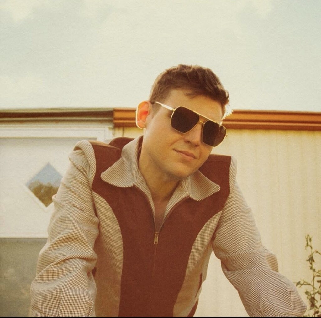 Adam Chaffins in sunglasses standing outside. A white wall and building are behind them.