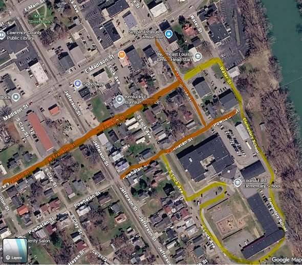 An aerial view of a town showing a main road with highlighted routes. Buildings and streets are visible.