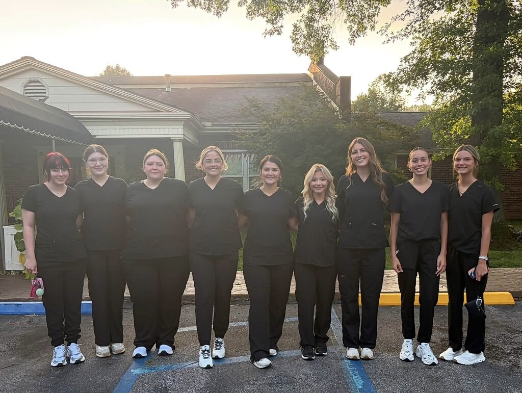 A group of women in matching black uniforms stand in a row outside a building.
