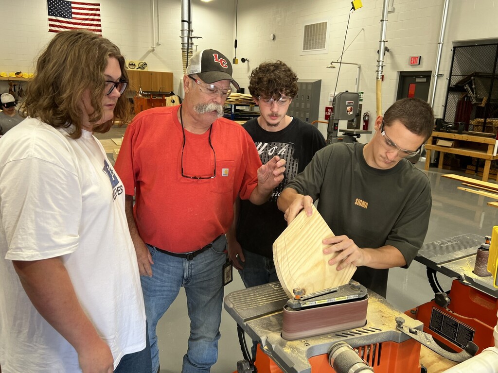 A group of men in a workshop; one is examining a piece of wood while another looks on.