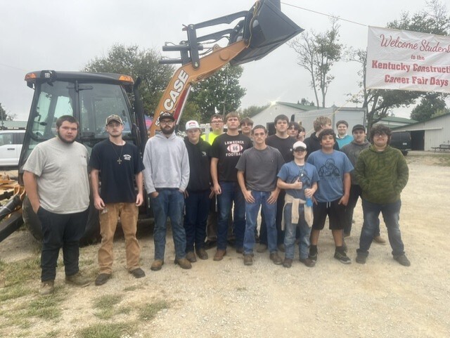 Group of people standing in front of a backhoe, with a banner reading "Welcome to Kentucky Construction Career Fair Day".