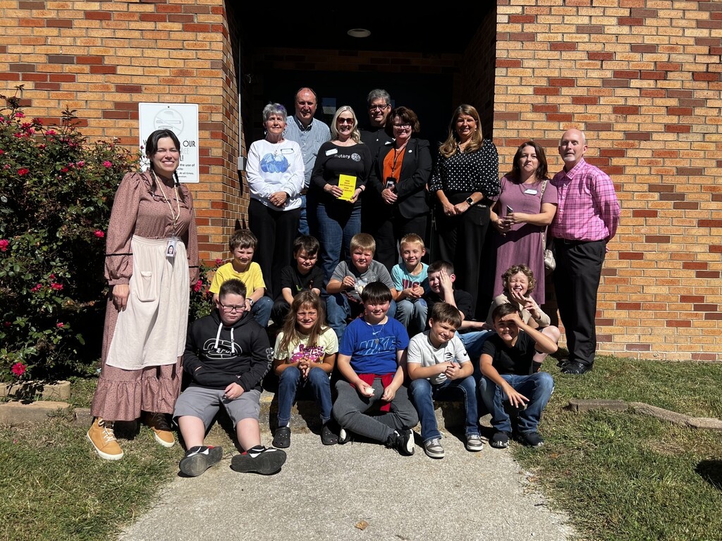 A group of people, including adults and children, standing and sitting in front of a brick building.