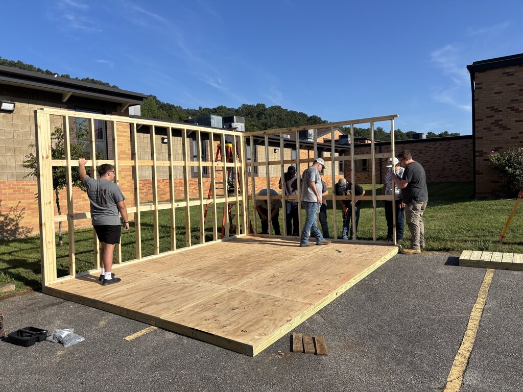 People working on a wooden structure on a concrete platform in a parking lot.