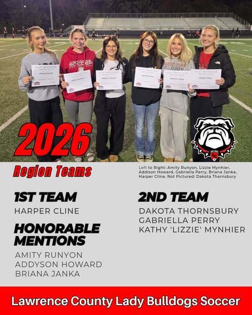 Six girls hold certificates on a sports field, one holding a red and white bulldog logo.