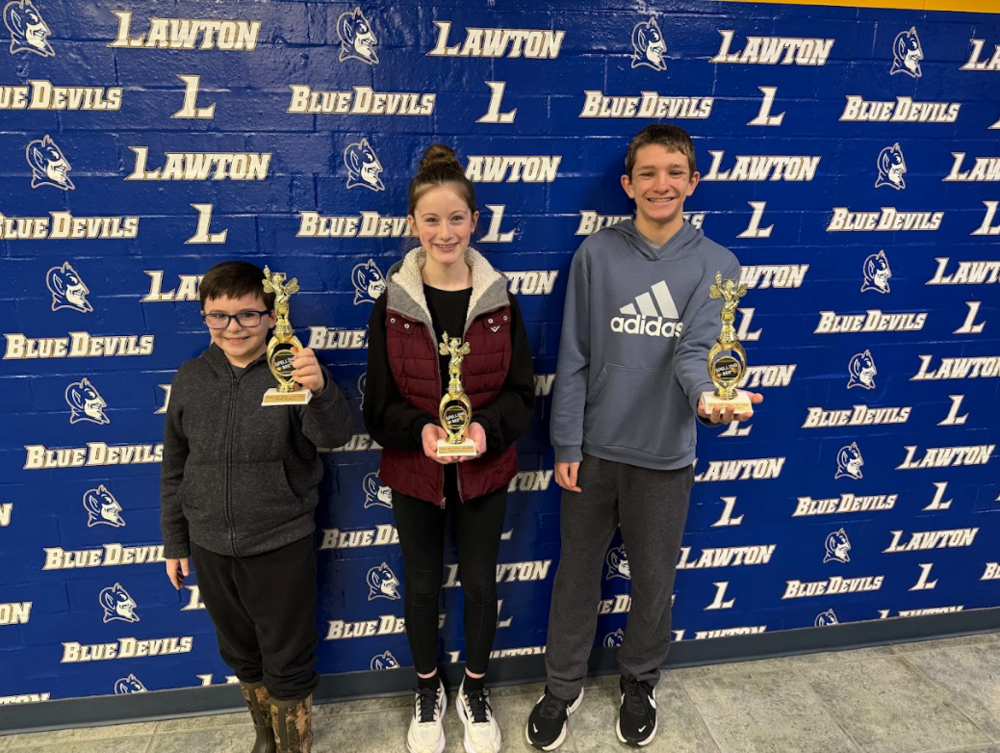 Three students stand with trophys for the spelling bee. 