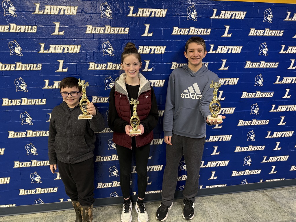 Three students stand with trophies for the spelling bee. 