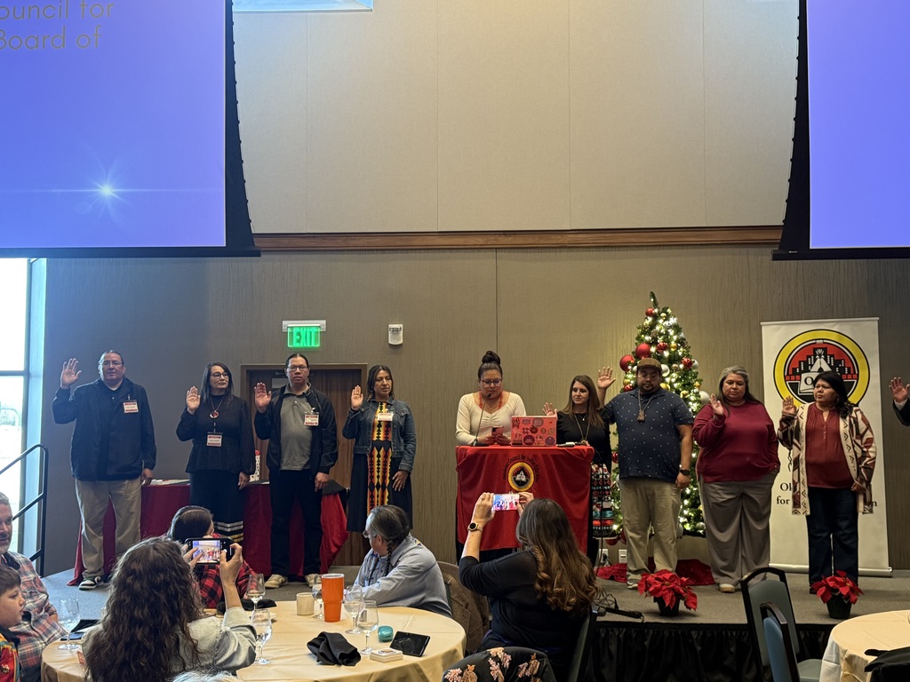 A group of people on a stage with a Christmas tree. Some are raising hands. A table with flowers and items sits in front.