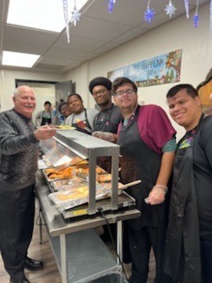 People in an indoor dining area, smiling at a buffet table with trays of food.