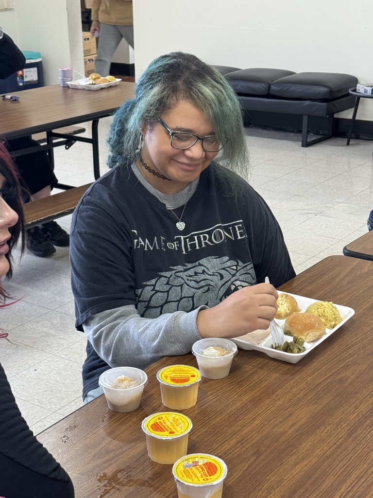A person  sits at a table eating with two people, food on a plate.
