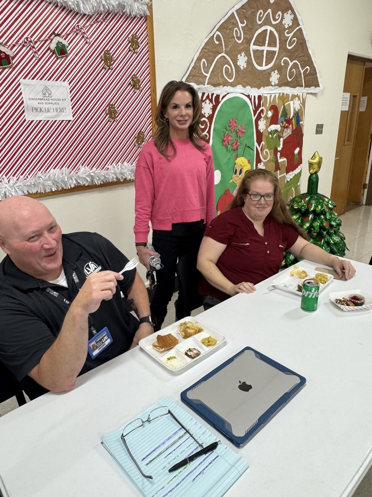 Three people seated at a table with food and a tablet. A Christmas-themed backdrop is behind them.